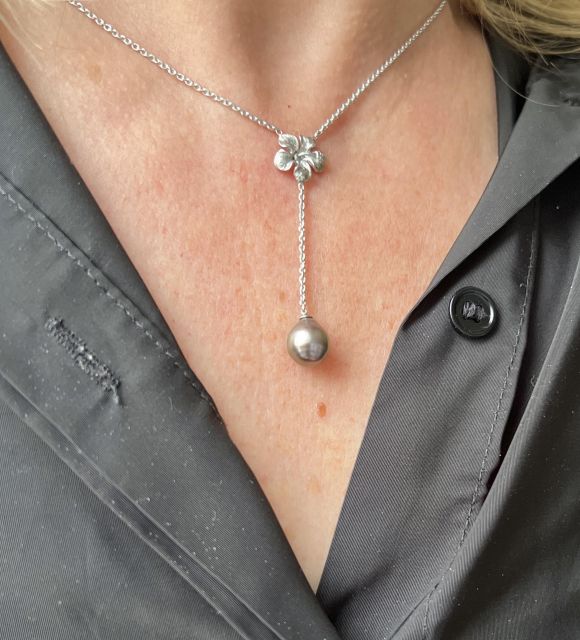 À la croisée du cou, une fleur s’épanouit. Un hibiscus finement ciselé, posé comme une offrande, laisse glisser la lumière jusqu’à une perle de Tahiti unique