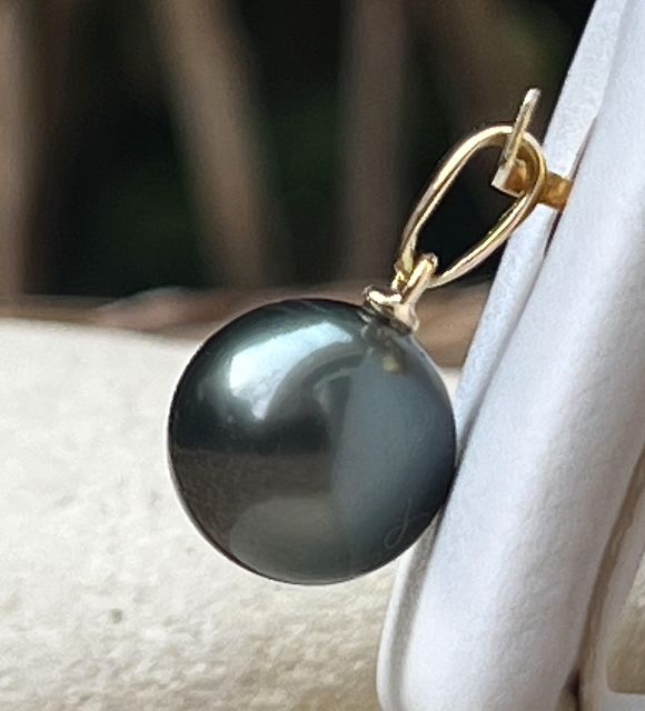 Suspendue à une bélière en or jaune 18 carats, cette perle d’exception révèle, sous certains rayons du soleil, de magnifiques reflets bleus, typiques des perles de Tahiti