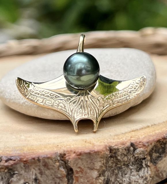 Une raie manta en or jaune 18 carats (4,85 g), gravée de motifs marquisiens, qui porte en son cœur une perle de Tahiti ronde TOP GEM de couleur outre-mer.
