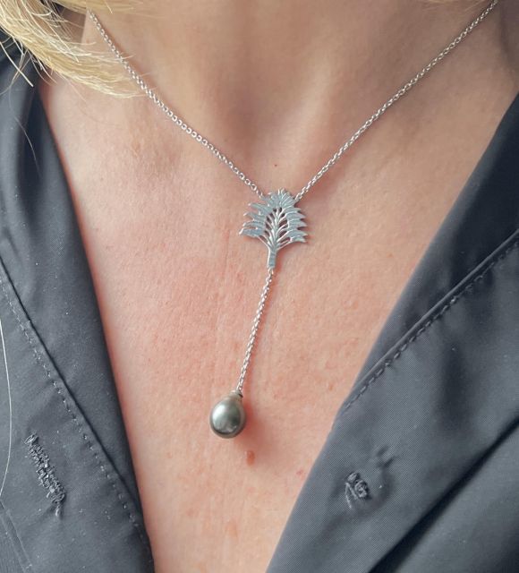 Une plaque d’argent martelé, une fleur de tiare Tahiti comme un murmure polynésien, et une perle gris-vert au lustre éclatant.